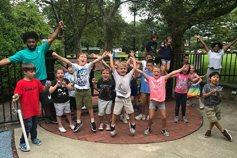 Children with arms in the air during Outdoor Camp.