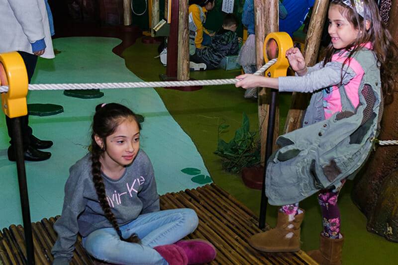 Two children crossing a bridge over a river in the Great Explorations Exhibit.