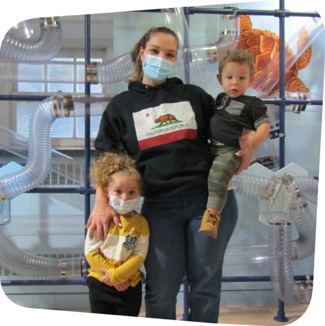 mom holding one child with one child by her side in front of air current exhibit