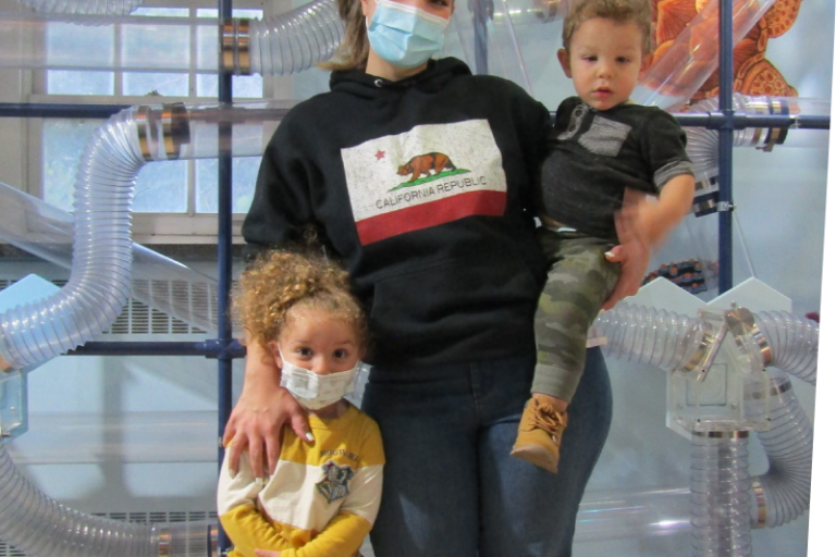 mom holding one child with one child by her side in front of air current exhibit