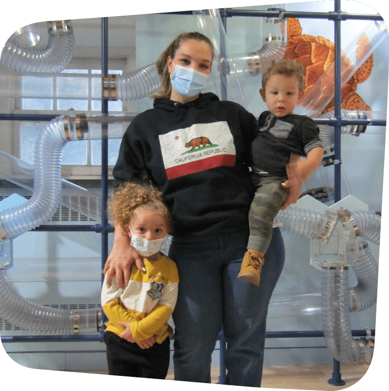 mom holding one child with one child by her side in front of air current exhibit