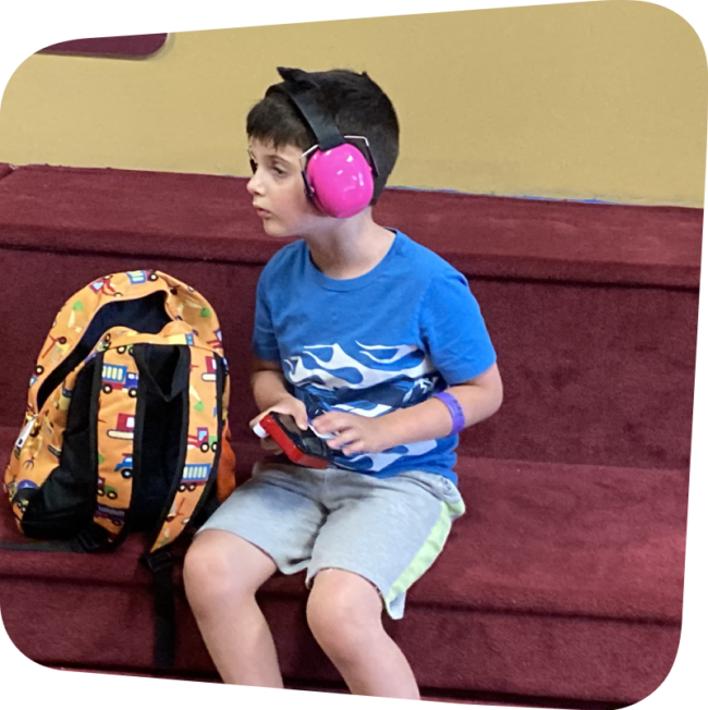 a child with pink headphones from the sensory toolkit on his head looking into the middle distance
