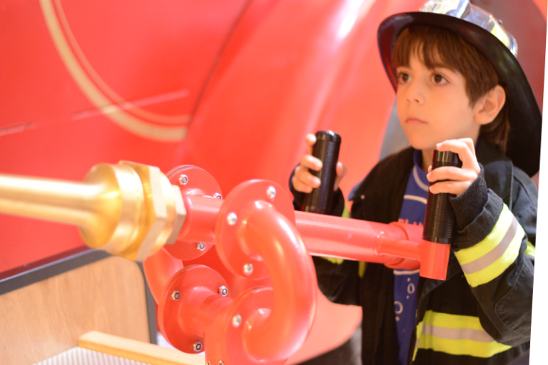 child in full fire fighter gear aiming the water gun in the Out Out Fire exhibit
