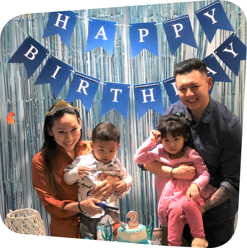 Mom and Dad holding children behind a birthday cake with a #2 candle in front of a Happy Birthday Banner