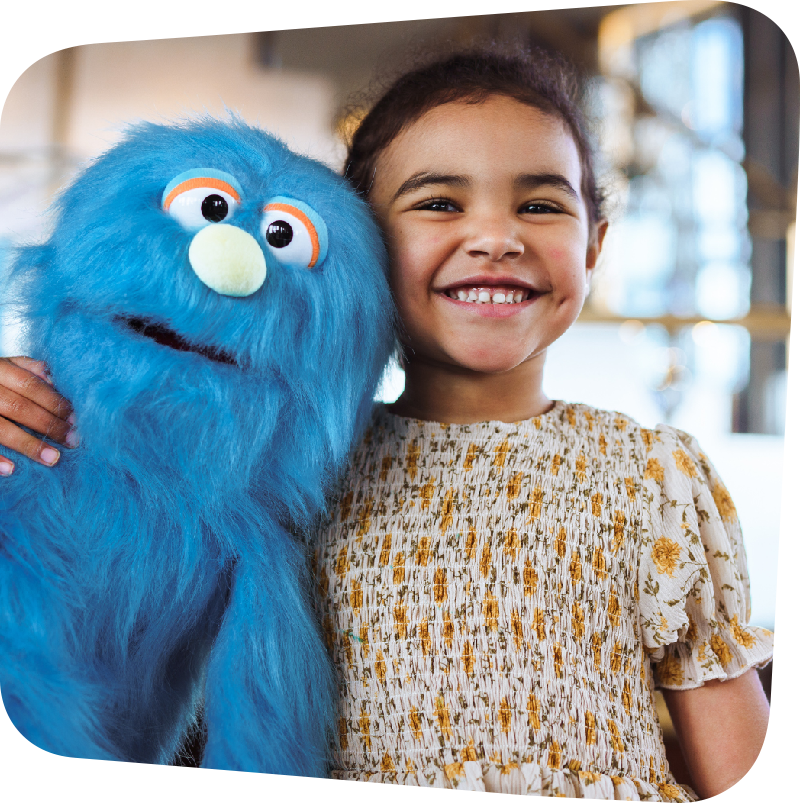 child smiling and hugging a blue monster like puppet