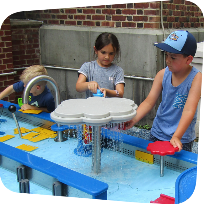 Three children playing at different stations of the water table in Sea of Boats an outdoor exhibit