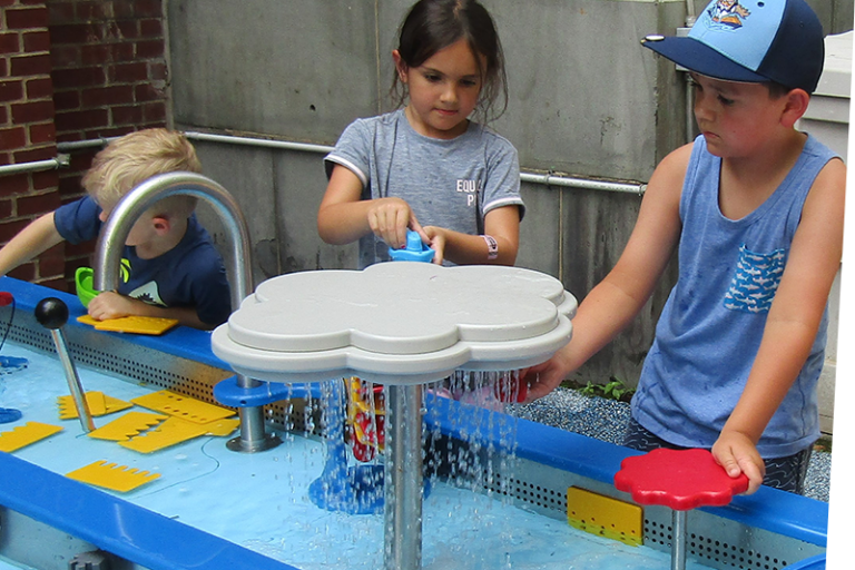 Three children playing at different stations of the water table in Sea of Boats an outdoor exhibit