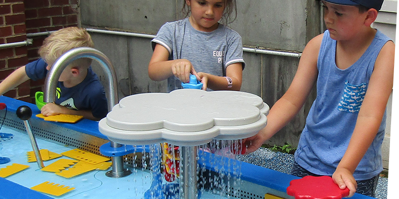Three children playing at different stations of the water table in Sea of Boats an outdoor exhibit