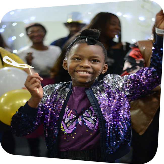 smiling child in a sparkly outfit in the midst of a baloon drop