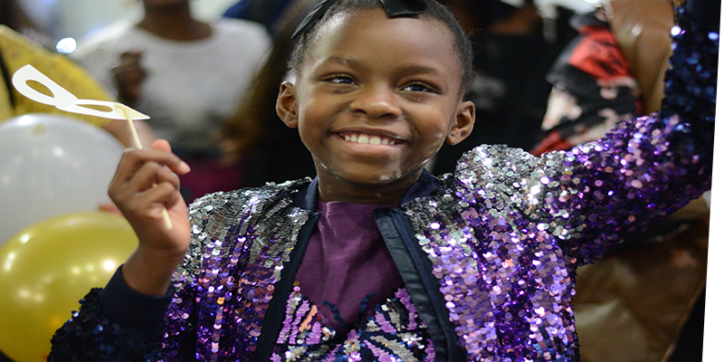 smiling child in a sparkly outfit in the midst of a baloon drop