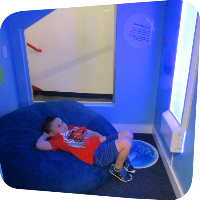 child reclining on a bean bag in a small room with dim lighting, looking at a glowing bubble wall feature
