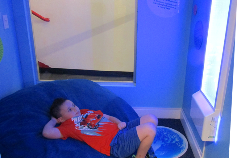 child reclining on a bean bag in a small room with dim lighting, looking at a glowing bubble wall feature