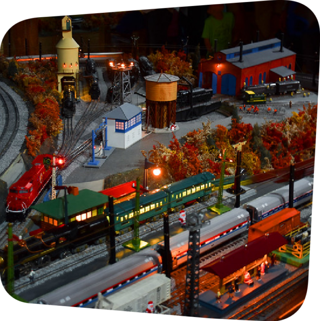 A model train village with trains in the station and the lamposts alight