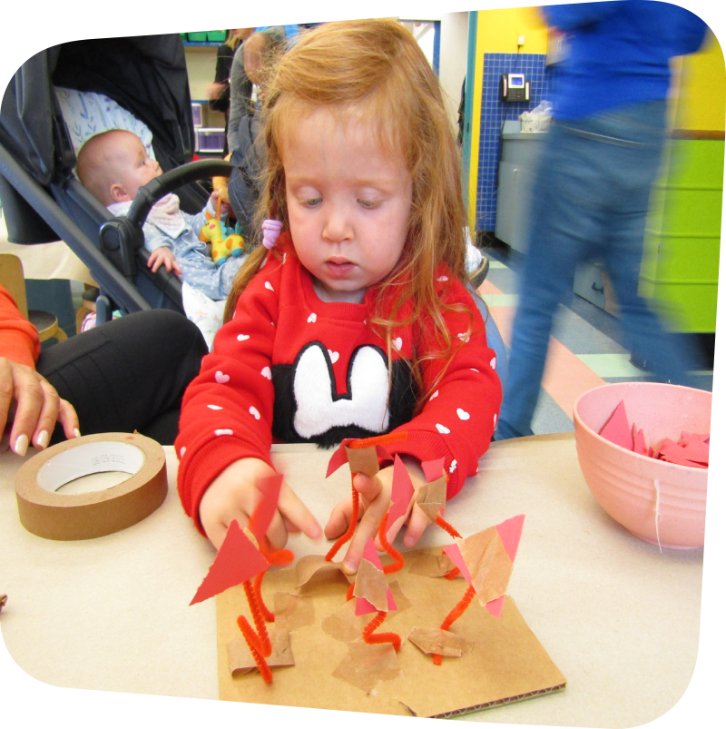 Child creating a sculpture with red pipe cleaners, construction paper and tape