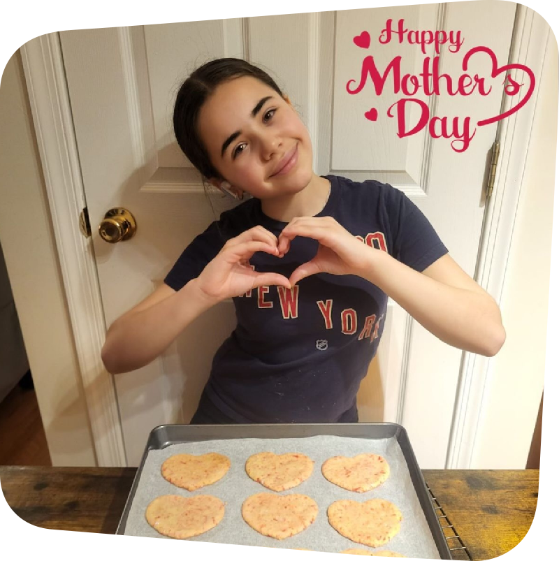 Maddison French making a heart shape with her hands, standing behind a try of freshly baked cookies