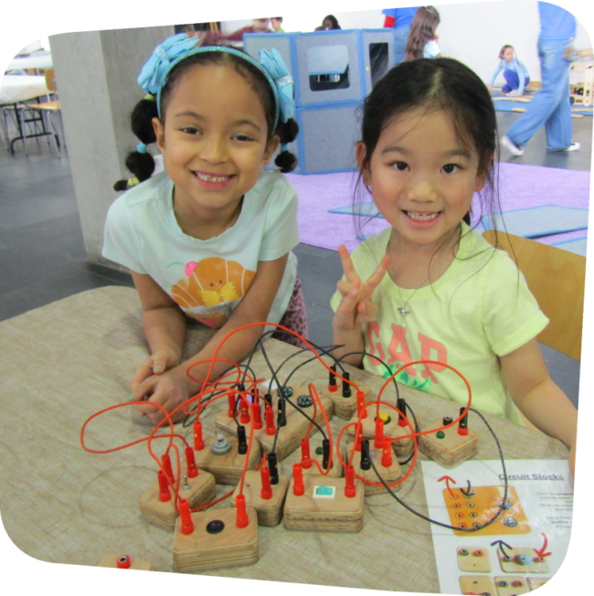 two smiling girls plaing with electrical connector blocks in the gallery at the Staten Island Children's Museum