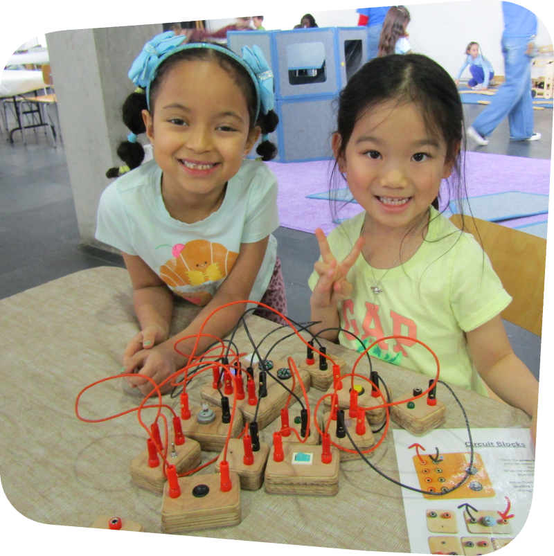 two smiling girls plaing with electrical connector blocks in the gallery at the Staten Island Children's Museum