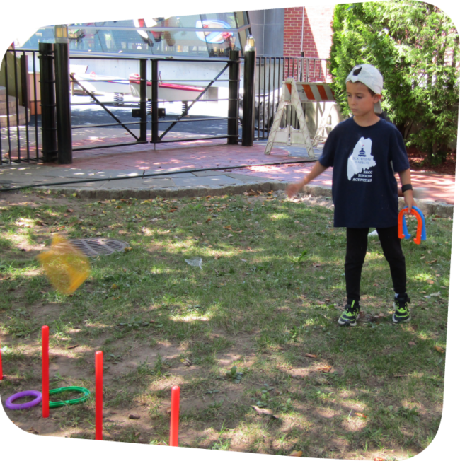 little boy tossing horseshoes at a target in the meadow at the Staten Island Children's Museum