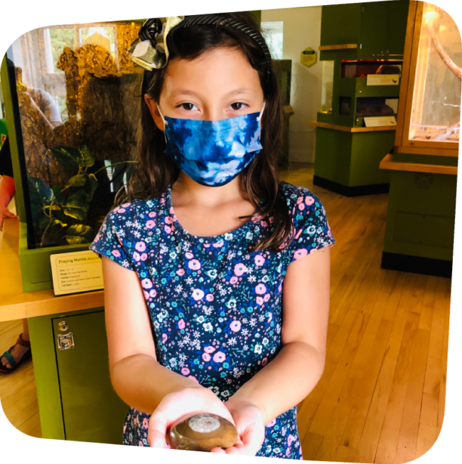 girl holding a circular shaped fossil in front of an exhibit in a museum
