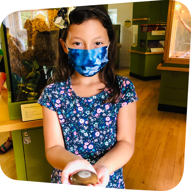 girl holding a circular shaped fossil in front of an exhibit in a museum