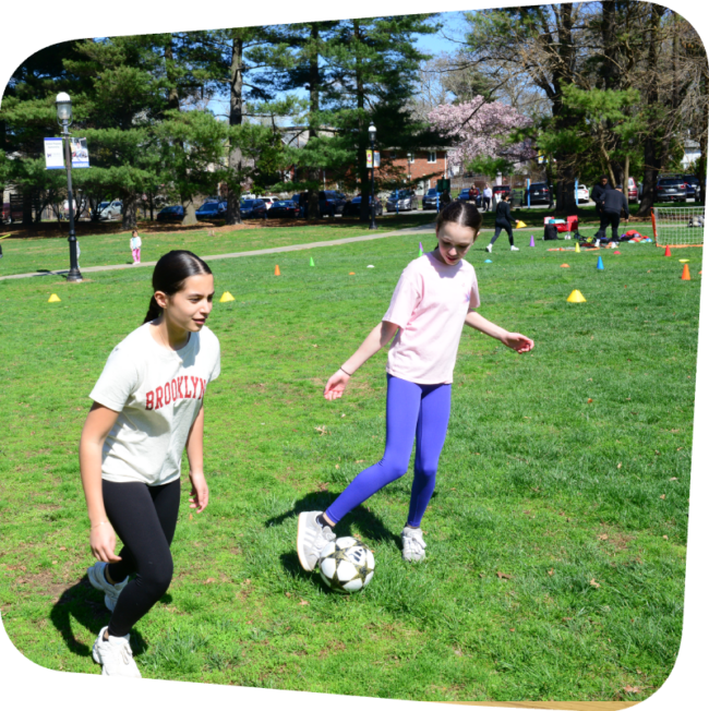 a girl passinga soccer ball to another girl during a soccer clinic outside of the Staten Island Children's Museum