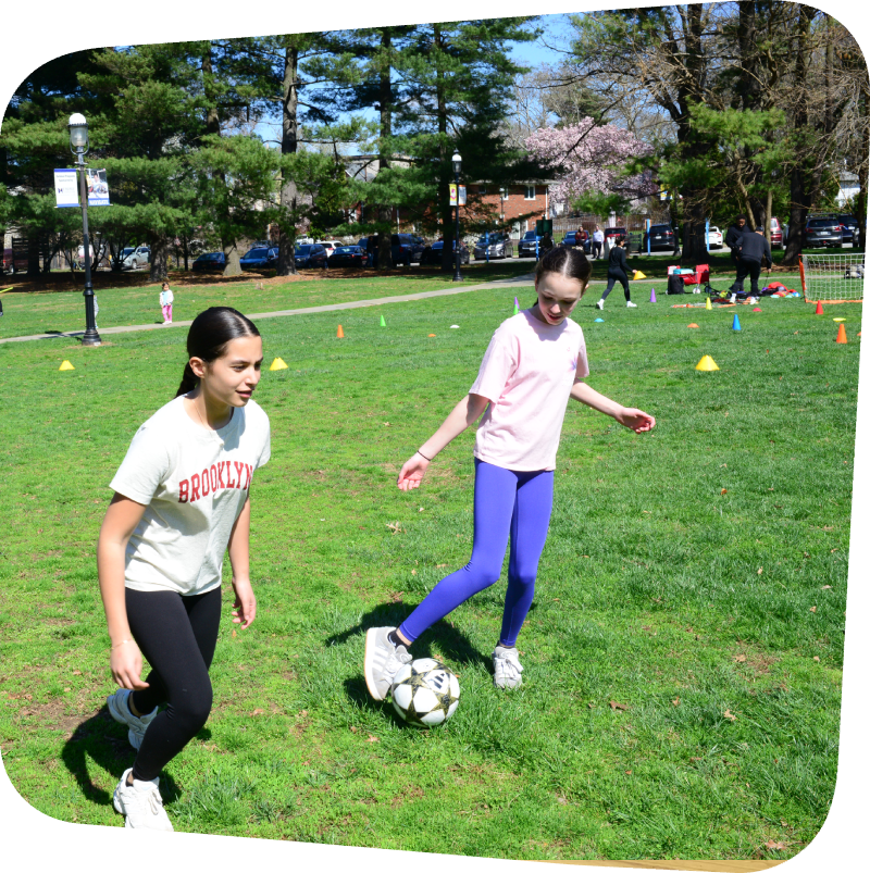 a girl passinga soccer ball to another girl during a soccer clinic outside of the Staten Island Children's Museum