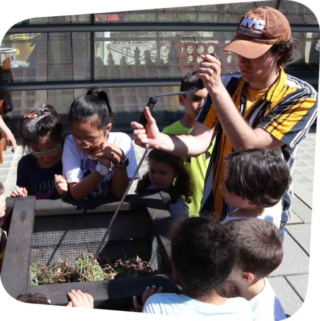 kids watching an compost instructor turn a crank in a compost bin in the Garden terrace at the Staten Island Children's Museum