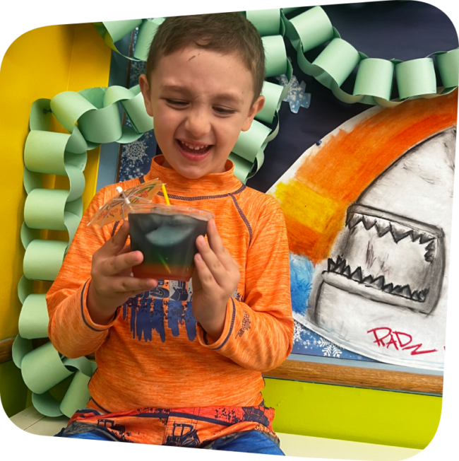smiling kid holding a cup of green and red lemonade in the art room at the Staten Island Children's Museum