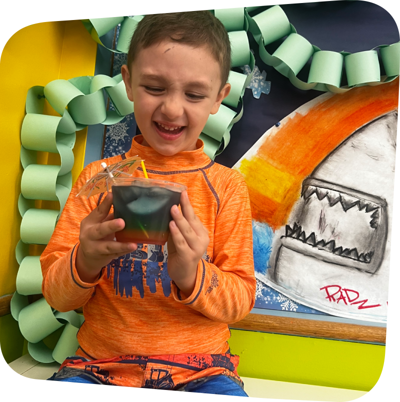 smiling kid holding a cup of green and red lemonade in the art room at the Staten Island Children's Museum