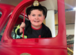smiling boy wearing a firefighters outfit standing in the door of ladder 11 exhibit at The Staten Island Children's Museum