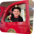smiling boy wearing a firefighters outfit standing in the door of ladder 11 exhibit at The Staten Island Children's Museum