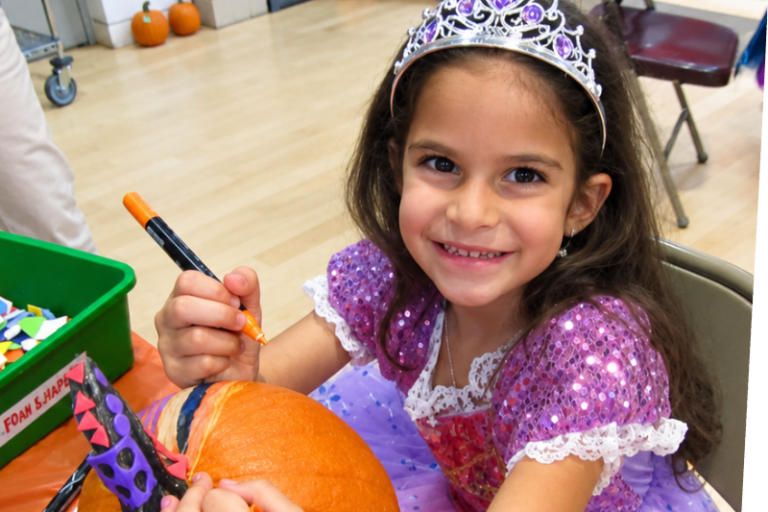 smiling girl decorating a pumpkin at the Staten Island Children's Museum halloween party