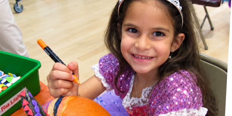 oct pr rhombus 2 smiling girl decorating a pumpkin at the Staten Island Children's Museum halloween party