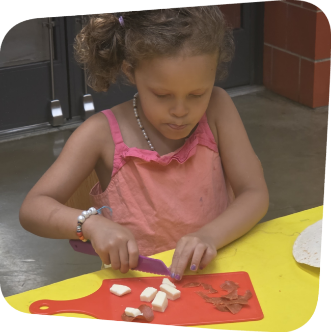 young girl chopping cheese into cubes in cooking class at the Staten Island Childen's Museum