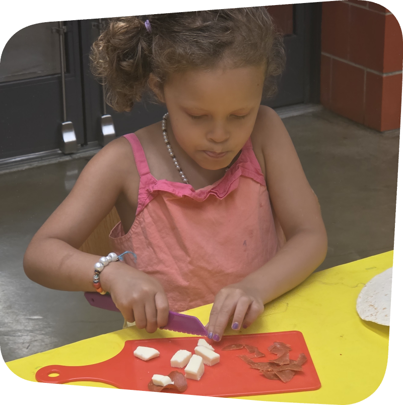 young girl chopping cheese into cubes in cooking class at the Staten Island Childen's Museum