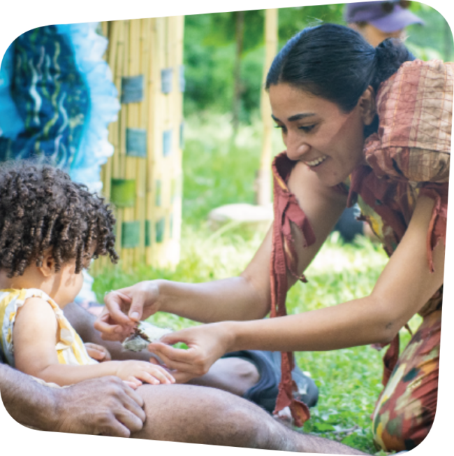 woman dressed in an earth tone outfit handing a small child a leaf